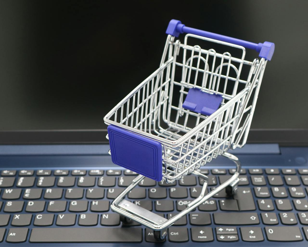 services-01 A mini shopping cart placed on a laptop keyboard, symbolizing online shopping and digital retail.